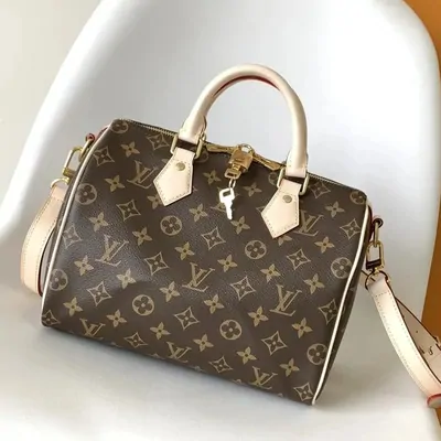 A brown monogram-canvas handbag with tan leather trim, rolled top handles and a padlock charm, standing on a white surface