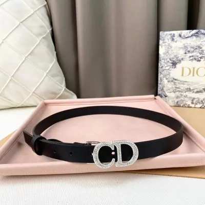 A black leather belt coiled inside a pink gift box, next to a quilted cushion and a printed card