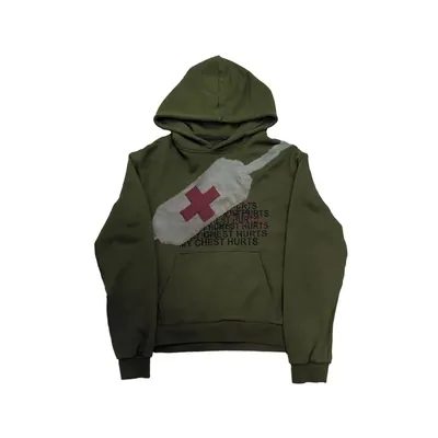 An olive-green pullover hoodie laid flat, with a printed graphic and a red cross across the chest