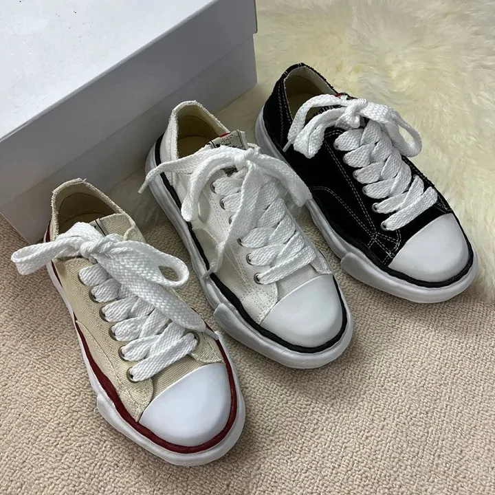 Two pairs of low-top canvas sneakers, one white and one black, laces left loose, photographed on a pale carpet beside an open box lid